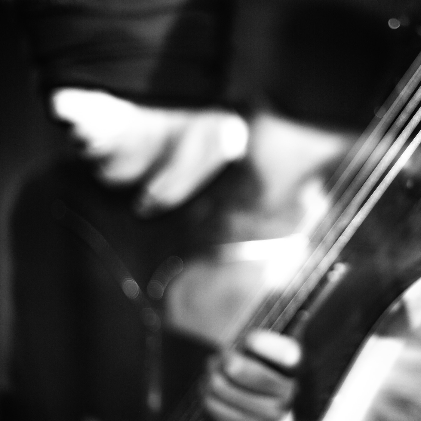 Album cover: hands on bass guitar strings, blurred black and white