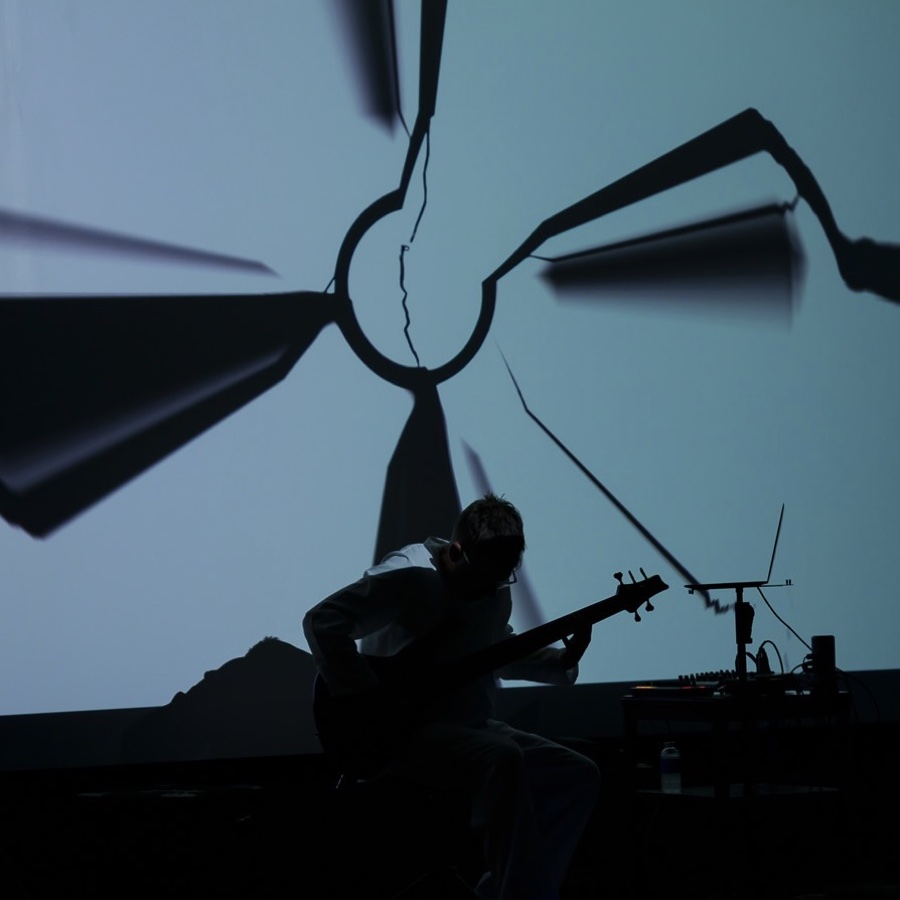 John von Seggern silhouetted with bass guitar against a projection screen